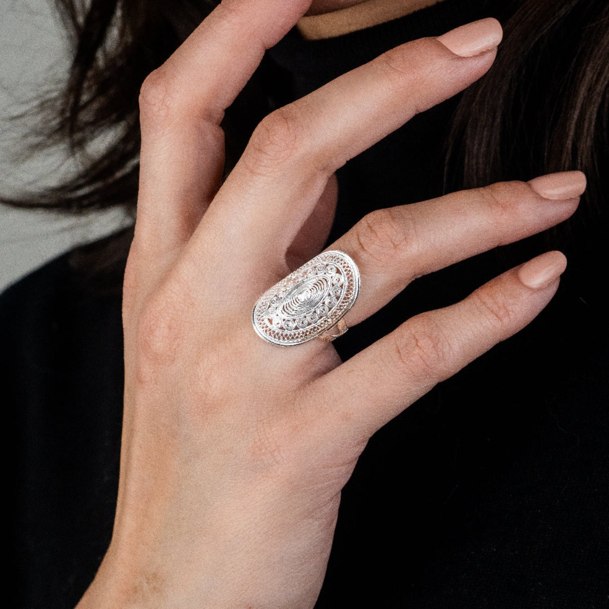 Close-up of a hand wearing a decorative silver ring against a dark background